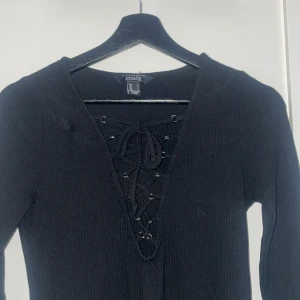 Svart klänning från Streetwear Society - Snygg svart klänning från Streetwear Society med lång ärm och snörning framtill. Den är ribbad och har en figurnära passform som framhäver silhuetten. Använt ändrat en gång så den är i mycket fint skick.