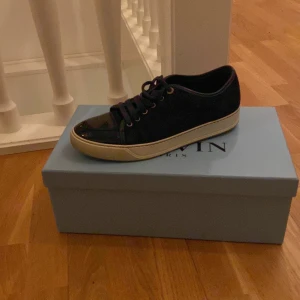 Svarta sneakers från Lanvin - Snygga svarta sneakers från Lanvin med glansig tå och snörning. Skorna har en vit sula och kommer i originalkartong med en Lanvin-dustbag. Perfekta för en stilren look.