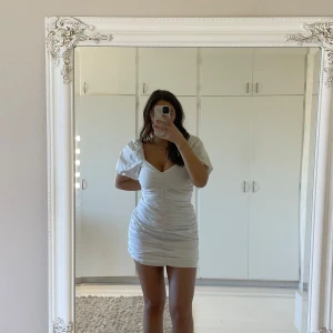 Vit kort klänning - Säljer min snygga vita minidress som jag hade på studenten! Perfekt till sommaren. Går att dra upp och ner de puffiga axlarna. Klänningen är rynkig och har samma material som en skjorta. 