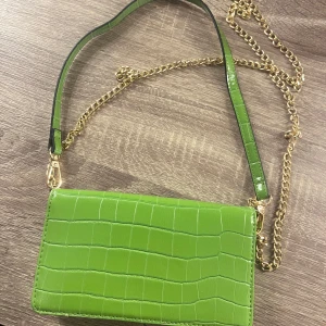 Grön axelväska med kedja från ASOS - Snygg grön axelväska i krokodilpräglat mönster från ASOS. Väskan har en guldfärgad kedja och en justerbar axelrem. Insidan har flera kortfack och stängs med en tryckknapp. Perfekt för att ge en färgklick till din outfit! Aldrig använd🌴