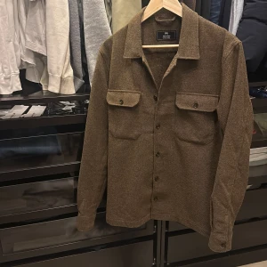 Brun overshirt från Matinique - Säljer en snygg brun overshirt från Matinique. Den har en klassisk krage och knäppning framtill med två bröstfickor med knappar. Perfekt för lager-på-lager-stil. Den är helt ny och aldrig använd utan prislapp. Säljer då den är lite liten på mig. Storleken är M. Passar M/L nypris la på ungefär 1600 mitt pris är nu endast 399!