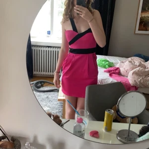 Rosa axelbandslös klänning - Snygg rosa klänning med svarta banddetaljer som korsar över bysten och midjan. Perfekt för en utekväll eller fest! Eller Valentinesday🔥😝🩷