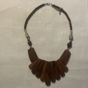 Halsband med trädetaljer - Unikt halsband med stora träbitar i olika former och storlekar. Halsbandet har även små bruna pärlor och silverfärgade detaljer. Perfekt för en bohemisk stil.