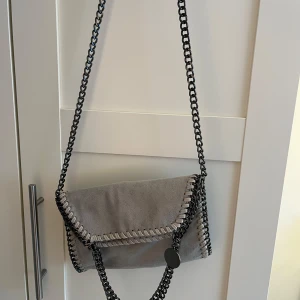 Grå axelväska med kedjedetaljer - Trendig väska som är köpt på en marknad i Spanien. Använd fåtal gånger💕💕