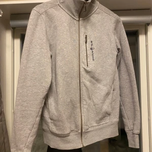 Grå zip tröja från Sail Racing - Snygg grå zip tröja från Sail Racing med dragkedja och hög krage. Perfekt för en casual look. Produkten är i rent nytt skick knappast använd och är i storlek XS. (Pris kan diskuteras har ej direkt ett fast pris på varan)