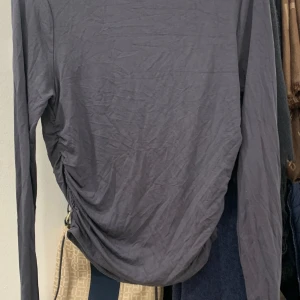 Grå långärmad topp med rynkade detaljer - Snygg grå långärmad topp med rynkade detaljer på sidorna. Perfekt för en stilren look. Tillverkad i mjukt material för extra komfort.