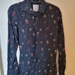 Blommig skjorta från Seven Seas - Snygg blommig skjorta från Seven Seas i mörk färg med små blommor i rött, vitt och blått. Skjortan är tillverkad i ren bomull och har en modern passform. Perfekt för en stilren look.