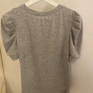 Grå topp från Shein - Säljer en grå topp från Shein med korta puffärmar. Tillverkad i mjukt polyestermaterial med en rund halsringning. Perfekt för en avslappnad stil. Helt oanvänd