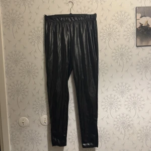 Svarta glansiga byxor - Snygga svarta glansiga byxor med elastisk midja. Perfekta för en trendig look. Passar bra till både vardag och fest.