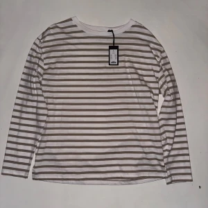 Randig långärmad tröja  - Säljer en stilren randig tröja med långa ärmar. Tröjan har en klassisk vit och beige färgkombination och är perfekt för en avslappnad look. Den är i nytt skick med etikett kvar.