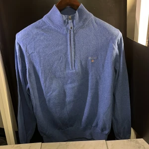 Blå halv zip från GANT - Säljer en stilren blå tröja från GANT i superkammad bomull. Tröjan har en halv dragkedja och ribbad krage, perfekt för en avslappnad men snygg look. Passar bra till både jeans och chinos. Denna är lite mindre än vad en ordinarie Medium är. Hör av er vid minsta fundering🙌