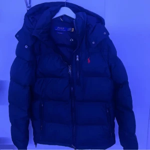 Mörkblå dunjacka från Polo Raulph Lauren - Säljer en mörkblå dunjacka från Polo Ralph Lauren i storlek S. Jackan är i ett utmärkt skick och har använts ett par gånger sedan den köptes i början av året. Den är stilren och passar både till vardag och finare tillfällen.  Priset är inte hugget i sten, så hör gärna av dig med frågor eller om du vill lägga ett bud.