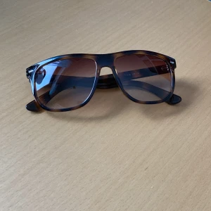 Bruna solglasögon från OneWear - Snygga solglasögon från OneWear med brunmelerat mönster och klassisk design. Som man ser på bild 3 så har några få bokstäver lossnat från fodralet. Solbrillorna har en super liten repa som är så liten att den ej går att fota och inget som märks vid användning!