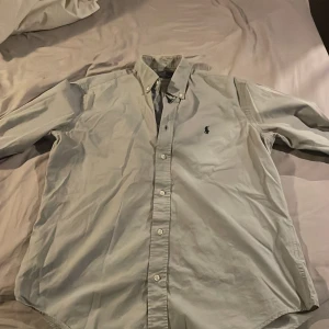 Grå skjorta från Polo Ralph Lauren - Säljer en stilren grå skjorta från Polo Ralph Lauren i slim fit. Skjortan har långa ärmar och klassiska knappar framtill. Perfekt för en elegant look. Skjortan är i storlek m men passar storlek s tror Jag.  Jag är 188 och väger 66 och den sitter bra i armarna men lite för kort