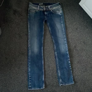 Blå jeans från Replay - Snygga blå jeans från Replay med en klassisk femficksdesign och dubbla knappar i midjan. Jeansen har en lätt tvättad look och smal passform som ger en modern stil. Perfekta för en avslappnad vardagslook.