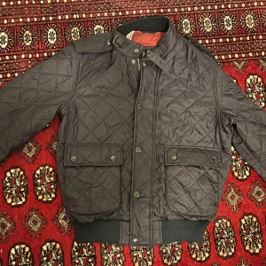 Mörk blå quiltad jacka från Barbour - Snygg blå quiltad jacka från Barbour med dragkedja och knappar. Jackan har långa ärmar och ribbade muddar. Perfekt för höst och vår. Knappt använd så den är i mycket gott skick.