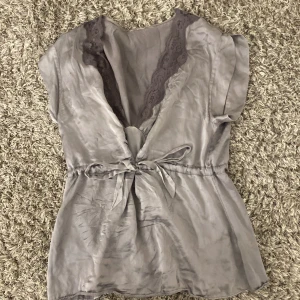 Grå blus med spetsdetaljer - Snygg grå blus med spetsdetaljer vid halsringningen och knytband i midjan. Perfekt festtopp!