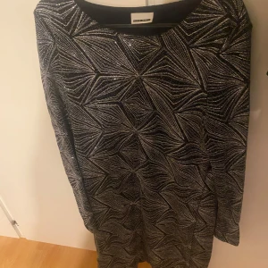 Svart och vit klänning från Noisy May - Snygg svart och vit klänning från Noisy May med ett geometriskt mönster. Klänningen har långa ärmar och en rund halsringning, perfekt för en stilren look.