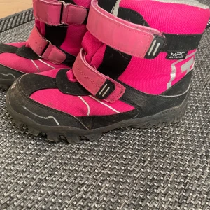 Rosa vinterkängor med kardborreband - Säljer ett par rosa vinterkängor med svarta och grå detaljer. De har praktiska kardborreband för enkel på- och avtagning. Perfekta för kalla vinterdagar.