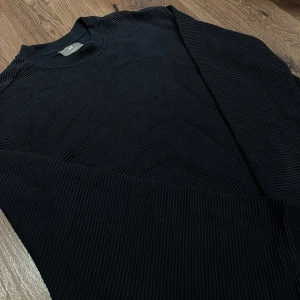 Mörkblå ribbad tröja från H&M - Säljer en stilren mörkblå ribbad tröja från H&M. Tröjan har långa ärmar och en klassisk rund halsringning. Perfekt för en stilren look. Helt ny med prislappen kvar. Nypris 279kr