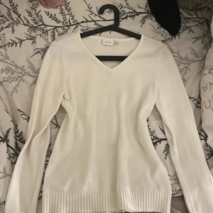 Vit tröja från Vila - Säljer en stilren vit tröja från Vila med v-ringning. Tröjan har långa ärmar och ribbade detaljer vid ärmslut och nederkant. Perfekt för en enkel och elegant look.