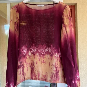 Blus från Maria Westerlind - Säljer en superfin blus  från Maria Westerlind i en härlig mix av vinröd och gult. Den har ett unikt batikmönster som verkligen sticker ut. Blusen är långärmad och perfekt för både höst och vår. Materialet känns lätt och luftigt, vilket gör den skön att bära. Endast använd ett par gånger. Se även annons för matchande kjol. 