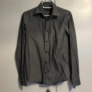 Grå randig skjorta från Tiger of Sweden - Säljer en stilren grå skjorta från Tiger of Sweden. Den har ett vit randigt mönster och är tillverkad i ett fint material som känns lyxigt. Perfekt för både vardag och fest! Skick 7/10. Frågor och funderingar? Tveka inte på att höra av dig.