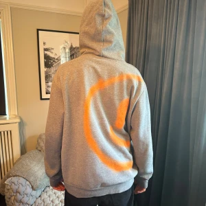 Grå hoodie med orange cirkelmönster - Säljer en grå hoodie med ett coolt grafittitryck på baksidan, hoodien är lite mörkare grå än vad den ser ut på den högra bilden. Sjukt cool till ett par jeans exempelvis. Hoodien är från ett samarbete mellan 4o1 och the seventh avenue, det finns endast ett exemeplar. 