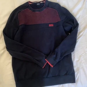 Mörkblå tröja från Hugo Boss - Säljer en snygg mörkblå tröja från Hugo Boss med röda detaljer. Tröjan har ett coolt mönster på bröstet och är långärmad. Perfekt för höst och vinter! Den är i bra skick och redo för nya äventyr. pris kan diskuteras 