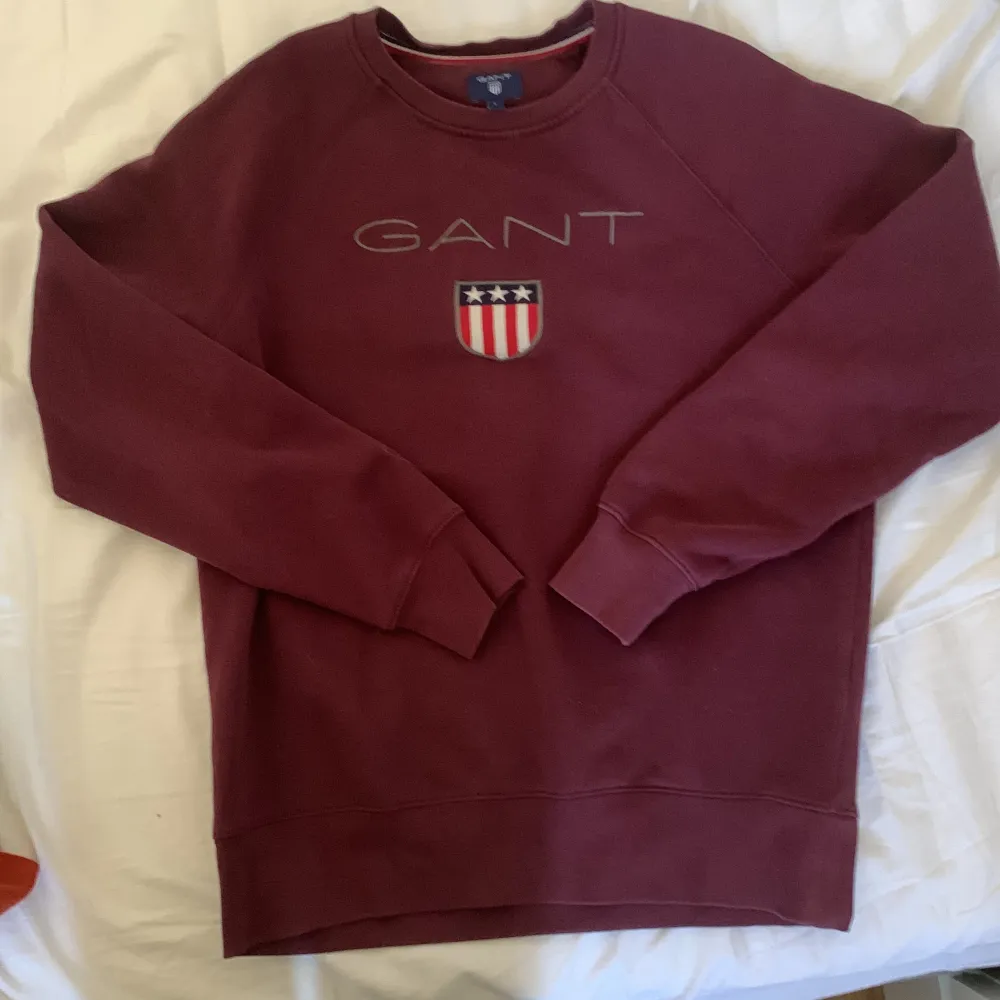 Säljer en snygg vinröd sweatshirt från GANT med deras ikoniska logga och ett coolt emblem på bröstet. Tröjan är långärmad och perfekt för både höst och vinter. Den är i storlek L och har en skön passform. Perfekt för en casual look eller när du vill vara bekväm men ändå stilren. pris kan diskuteras!. Tröjor & Koftor.