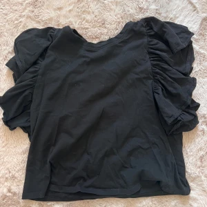 Svart topp med volangärmar - Säljer en snygg svart topp från zara med volangärmar. Perfekt för både vardag och fest. Toppen är i ett mjukt och bekvämt material, och har en normal passform. Den är kortärmad och har en enkel men stilren design.