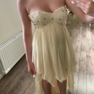 Champagnefärgad klänning från Nelly Eve - Säljer en superfin champagnefärgad klänning från Nelly Eve. Den är axelbandslös och har en vacker snörning i ryggen. Klänningen är dekorerad med små glittriga detaljer på överdelen och har en härlig flowy kjol. Säljer då den är förliten för mig. Perfekt för fest eller bal! 💫