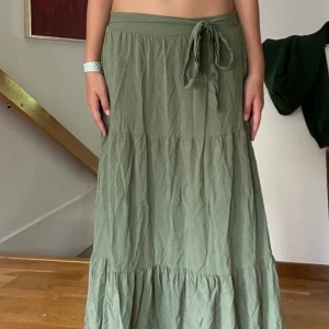 Grön långkjol från Amisu - Säljer en superfin grön långkjol från Amisu i storlek S (EU 36). Kjolen har en knytning i midjan och är perfekt för både vardag och fest. Den är tillverkad i ett lätt och bekvämt material som gör den skön att bära hela dagen. Passar perfekt till sommaren eller våren!