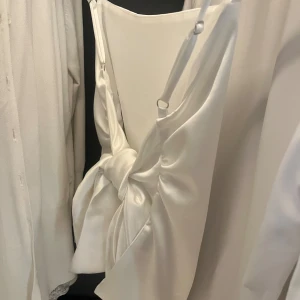 Vit satin topp från Zara - Säljer en elegant vit Topp från Zara i satinmaterial. toppen har justerbara axelband och en jättefin rosett i ryggen som ger en lyxig känsla. Perfekt för festliga tillfällen eller en speciell kväll ute. Ny och oanvänd med lappem kvar!!