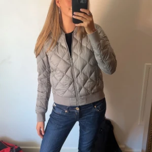 Grå quiltad bomberjacka från Uniqlo - Säljer en snygg och lätt grå bomberjacka från Uniqlo. Jackan är quiltad och har en dragkedja framtill. Den är perfekt för höst och vår med sin vattenavvisande funktion. Superbekväm och stilren!