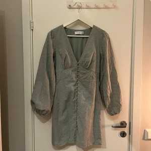Vila grön klänning - En vacker klänning med långa ärmar och en v-ringning. Klänningen har en knapprad framtill och en elastisk midja. Den är i en mjuk och bekväm kvalitet. Nypris: 799 kr.