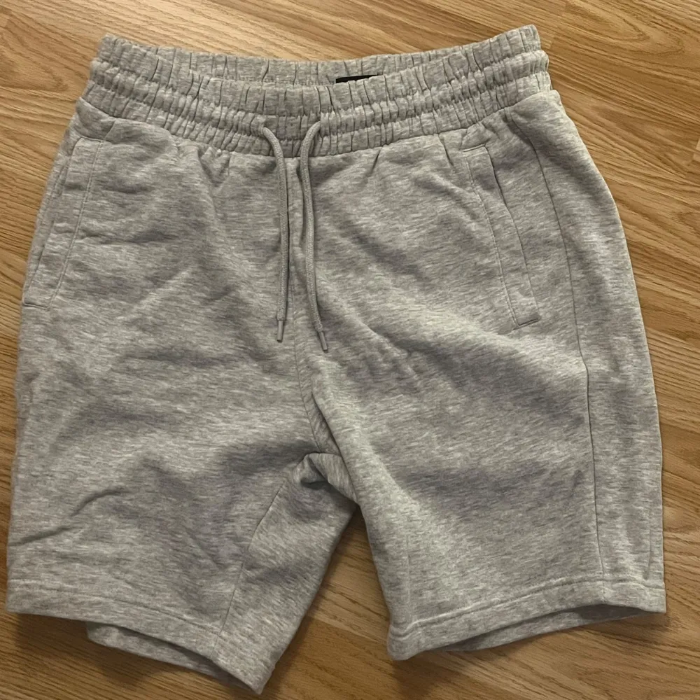 Säljer två par shorts från H&M i storlek M. Ett par är svarta och det andra är grått. Båda har en regular fit och är perfekta för en avslappnad stil. De har elastisk midja med dragsko för justerbar passform. Materialet känns mjukt och bekvämt, perfekt för sommardagar eller träning.. Shorts.