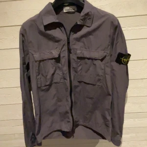 Stone island Overshirt  - Säljer min Stone island overshirt i en blå/grå färg då den har blivit för liten, overshirten är sparsamt använd och är i bra skick. Storlek:M Skick:9/10 Pris kan diskuteras vid snabb o smidig affär