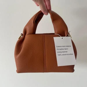 Brun väska  - Jättefin brun väska med prislapp kvar då jag fick hem den men kunde ej skicka tillbaka. Alltså helt oanvänd. Köpt på en engelsk hemsida för 600kr Långt band tillkommer.