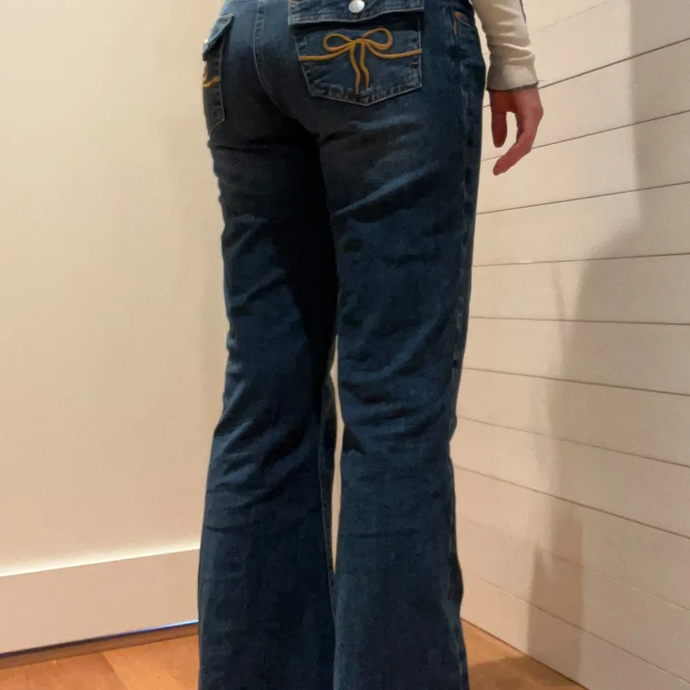 Säljer ett par snygga blå bootcut jeans med coola broderade detaljer på bakfickorna. De har en låg midja och är perfekta för en avslappnad stil. Jeansen är i bra skick och passar perfekt till både vardag och fest.. Farkut & Housut.