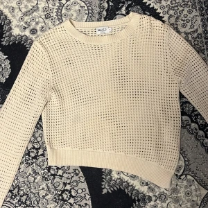 Beige stickad tröja från NA-KD - Säljer en beige stickad tröja från NA-KD med ett luftigt hålmönster. Tröjan är croppad och har långa ärmar. 