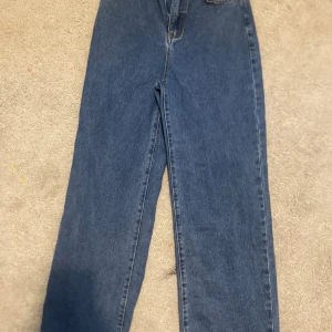 Blå jeansbyxor - Klassiska blå jeansbyxor med hög midja och rak passform. Perfekta för en avslappnad stil. De har fem fickor och en dragkedja framtill.