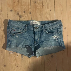 Lågmidjade jeansshorts från Hollister - Snygga blå jeansshorts från Hollister med slitna detaljer och fransiga kanter. Perfekta för en avslappnad sommarlook. Pris kan diskuteras💕