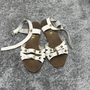Vita sandaler med spännen - Snygga vita sandaler med flera remmar och dekorativa spännen. Perfekta för sommarens varma dagar. Sandalerna har en brun sula och justerbara remmar för bästa passform.