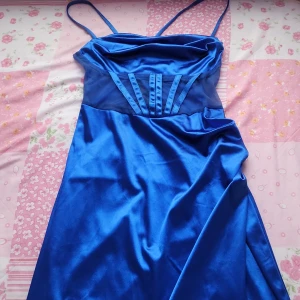 Blå axelbandslös klänning - Snygg blå axelbandslös klänning i satin med smala axelband och snörning i ryggen. Perfekt för en bal. Klänningen har en elegant slits och en figurnära passform.
