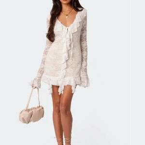 Vit spetsklänning med volangdetaljer - Säljer en elegant vit spetsklänning med långa ärmar och volangdetaljer. Klänningen har en v-ringad design med knyt framtill och är perfekt för en stilfull look. Från edikted. Nysprs: 1450 kr. Aldrig använd. Storlek s