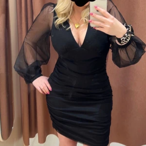 Svart klänning med transparenta ärmar - Elegant svart klänning med v-ringning och transparenta långa ärmar, Från gina tricit. Perfekt för en kväll ute. Den har en tight passform som framhäver figuren.