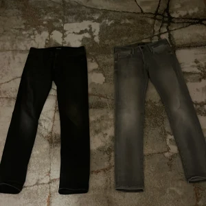 Svarta och grå jeans från Baywear - Två par jeans från jack&jones i olika färger. Ett par är svarta och det andra är grått. Båda har en klassisk femficksdesign och knappgylf. Perfekta för en stilren look. Båda jeansen är i storlek 28/30.