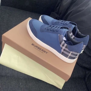 Burrbery skor - Snygga blå sneakers från Burberry med klassiskt rutigt mönster på sidorna. Skorna har en vit sula och snörning framtill. Perfekta för en stilren look. Skorna är i nytt skick använda 5 gånger typ . 