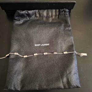 Silverarmband från Saint Laurent - Elegant silverarmband från Saint Laurent med rektangulära länkar och en diskret logotypbricka. Oanvänd i originalförpackning.